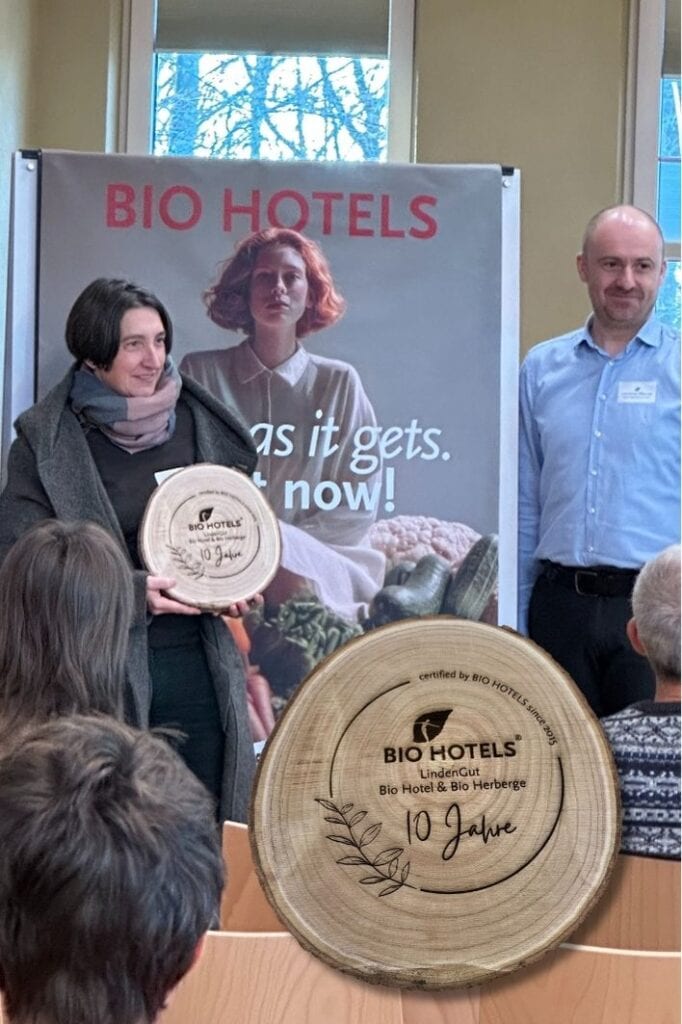 Übergabe der Holzplakete zum 10-jährigen Jubiläum des LindenGuts bei Bio Hotels vor dem neuen Banner der Bio Hotels