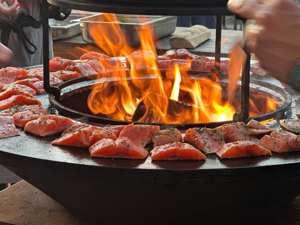 Ofyr mit Flammen in der Mitte. Auf der Grillplatte liegen mehrere Stücke Lachs.